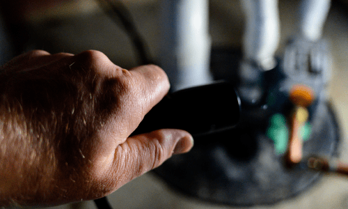 Plumber’s hand using a tool near plumbing pipes