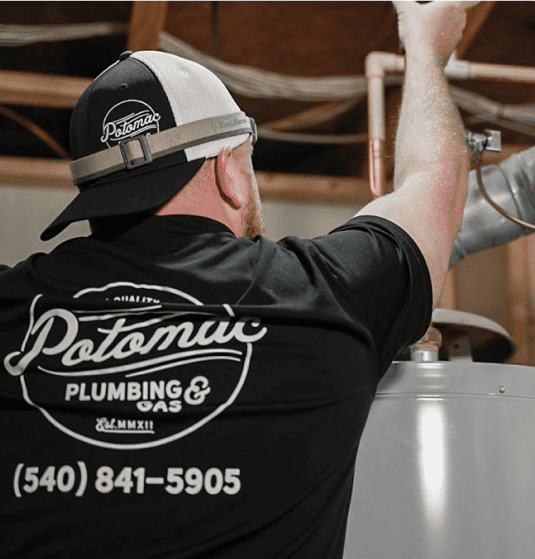 Plumber working on a water heater wearing Potomac Plumbing & Gas shirt