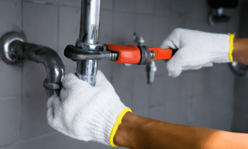 Hands fixing pipe with wrench.